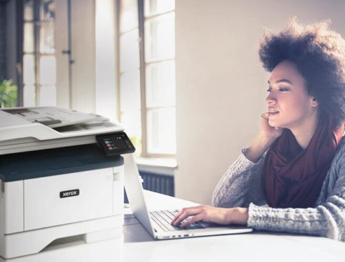 Jovem a trabalhar no seu computador ao lado de uma impressora multifunções Xerox® B315.