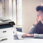 Ung kvinde arbejder ved sin computer ved siden af en Xerox® B315 multifunktionsprinter.