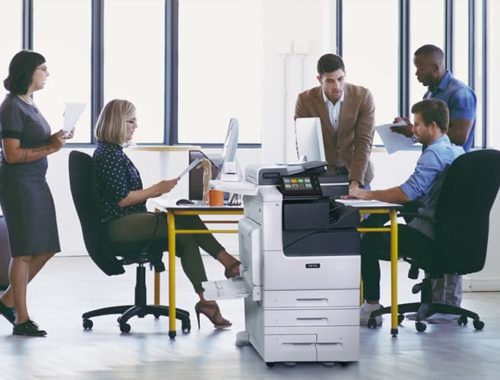 Equipa que trabalha num escritório com papéis impressos e a impressora multifunções a cores Xerox® Série VersaLink® C7100