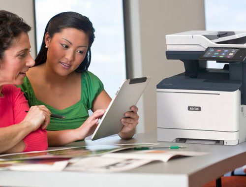 Duas mulheres usando um tablet em frente a uma impressora multifuncional Xerox VersaLink B415