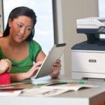 Dos mujeres usando una tableta frente a una impresora multifuncional Xerox® VersaLink® B415