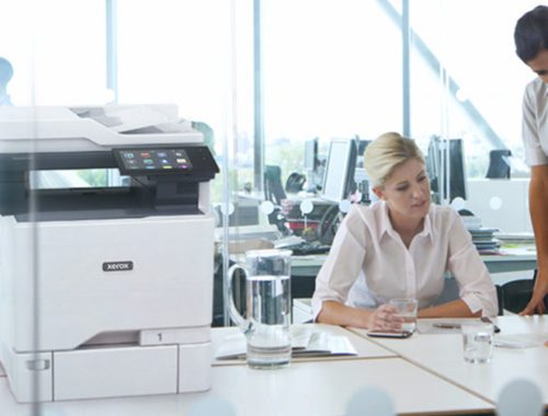 To kvinder arbejder på et kontor ved siden af en Xerox® VersaLink® C625-multifunktionsfarveprinter