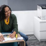 Mulher sorridente em um escritório ao lado da impressora colorida Xerox® VersaLink® C620