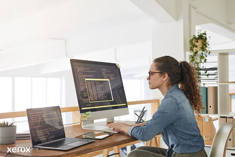 Uma mulher na sua secretária, ocupada com um computador e um portátil, a demonstrar produtividade num espaço de trabalho moderno. Uma mulher na sua secretária, ocupada com um computador e um portátil, a demonstrar produtividade num espaço de trabalho moderno.