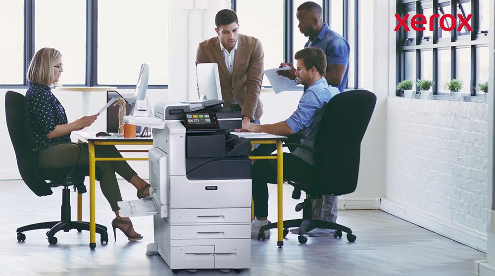 Büroangestellte arbeiten neben einem Xerox-Drucker zusammen.