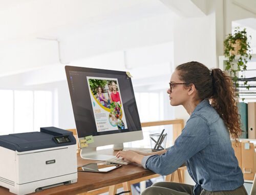 A woman seated at a desk, focused on her work, with a Xerox® C320 Colour Printer