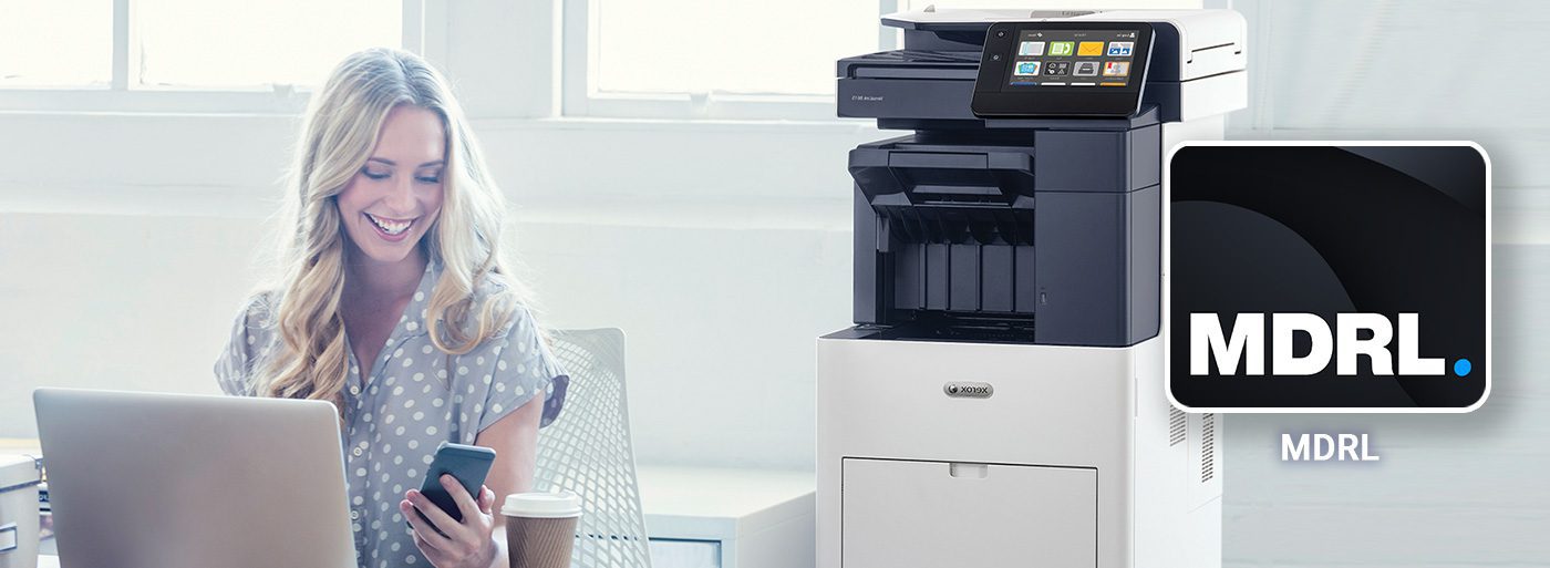 My Digital Registered Letter Application Smiling woman working at a computer and mobile phone next to a Xerox printer