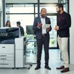 Two men in an office setting discussing something on a tablet beside a Xerox® AltaLink® C8200 Series Colour Multifunction Printer Two men in an office setting discussing something on a tablet beside a Xerox® AltaLink® C8200 Series Colour Multifunction Printer