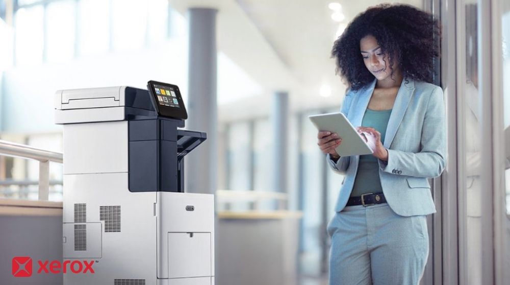 A person stands next to a Xerox VersaLink B605 multifunction printer, looking at and interacting with a tablet device, illustrating how ConnectKey enables mobile interaction with the printer.