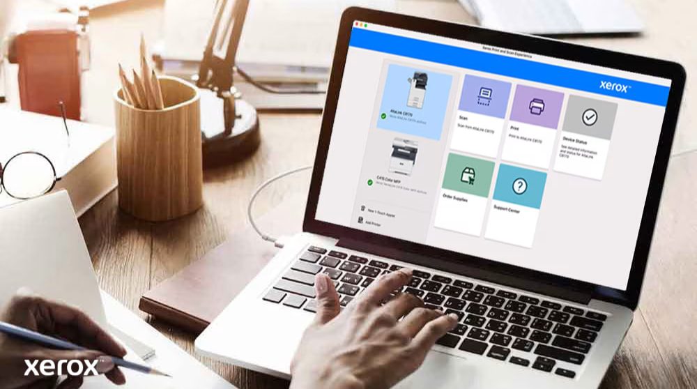 Xerox® Print- en scanervaring: intuïtieve bediening Iemands handen liggen op het toetsenbord van een laptop en op het scherm wordt de interface van Xerox Print and Scan Experience weergegeven, met opties zoals Scannen, Afdrukken, Apparaatstatus, Benodigdheden bestellen en Ondersteuningscentrum, wat wijst op een gebruiksvriendelijke bediening.