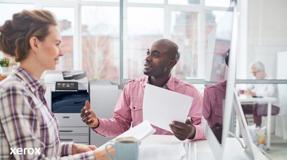 Xerox® Workplace Cloud e Suite: Gerenciamento Centralizado de Frotas Uma pessoa analisa dados na tela de um laptop, com uma sobreposição digital de vários ícones de dispositivos (impressoras, dispositivos móveis) e linhas conectadas, simbolizando o gerenciamento centralizado de frotas para o Xerox Workplace Solutions.