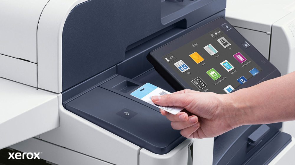 Una mano sostiene una tarjeta de seguridad y la escanea cerca del lector de tarjetas de una moderna impresora multifunción Xerox con una gran pantalla táctil que muestra varios íconos de aplicaciones.